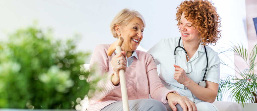 Friendly relationship between smiling caregiver in uniform and happy elderly woman. Supportive young nurse looking at senior woman. Young caring lovely caregiver and happy ward